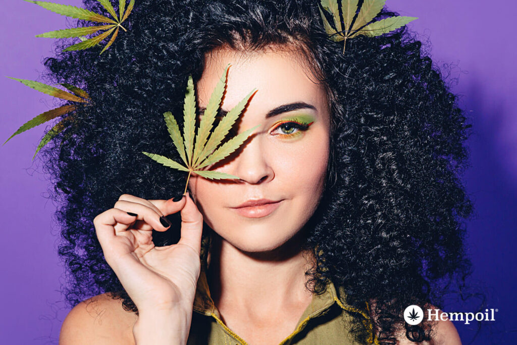 Woman holding cannabis leafs on hair face.